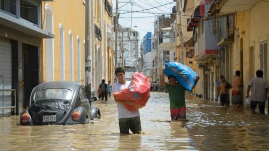 Dos vendedores cargan costales con mercancía por una calle inundada por el río Piura en Perú. Foto: EFE.