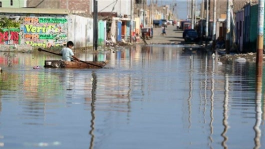 Un niño damnificado se desplaza sobre una pequeña balsa por una calle inundada de la ciudad de Huarmey en la región costera de Ancash (Perú). Foto: EFE.