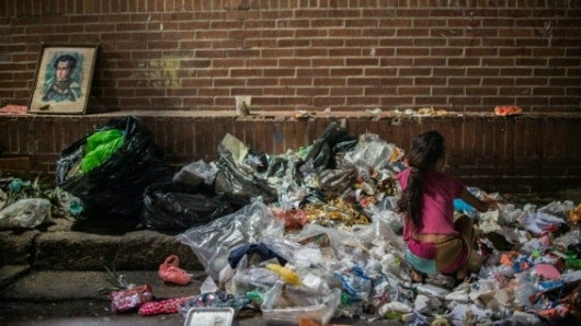 Una niña busca alimentos en la basura en una calle de Caracas. Foto: AFP.